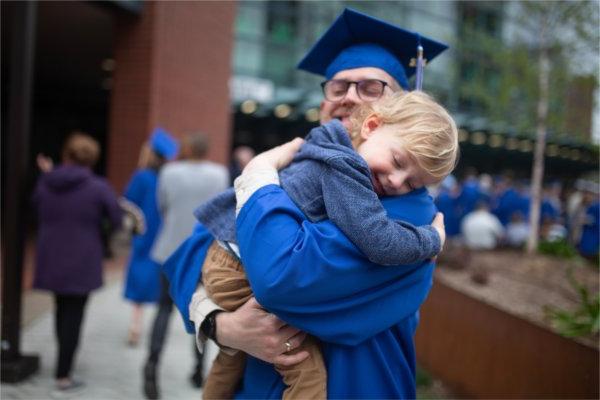 毕业典礼后，一位毕业生紧紧地拥抱着一个孩子. 