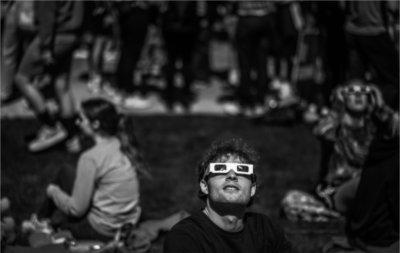 一个人戴着特殊的日食眼镜，坐在地上看着天空. 其他人坐在这个人的后面.