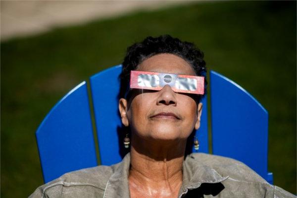 一个戴着特殊日食眼镜的人把头靠在一张蓝色椅子的靠背上，望向天空.