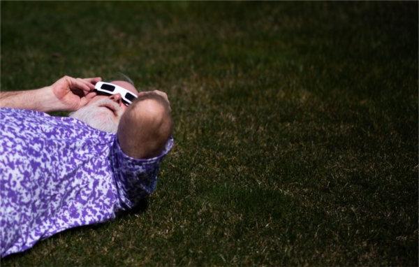 一个躺在地上的人在观看日食时把特殊的眼镜顶在头上.