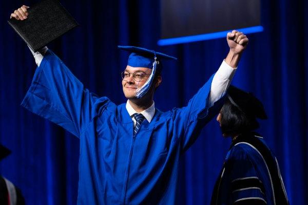 一名毕业生在台上高举双手庆祝毕业证书.
