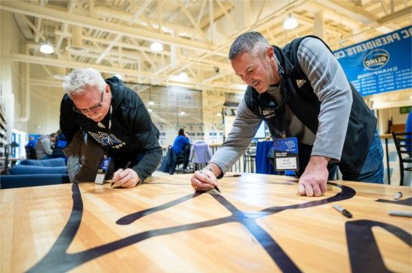 GVSU head football coach Scott Wooster, 左, signs a banner congratulating President 名誉教授托马斯?. 哈斯 for the Fieldhouse Arena basketball court being named in his honor. 