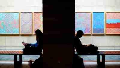 Two college students are silhouetted as they do school work in front of framed art. 