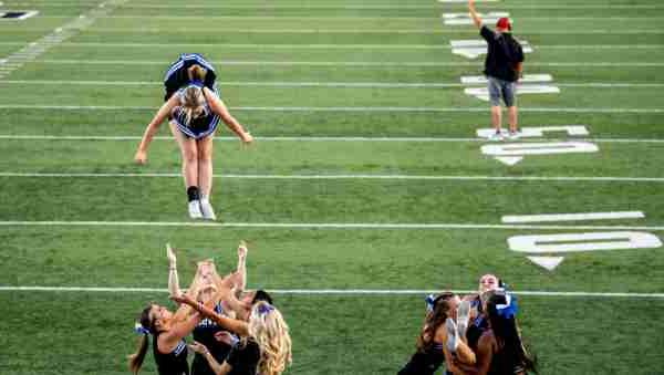 A cheerleader is tossed into the air along the sidelines of a football field.  