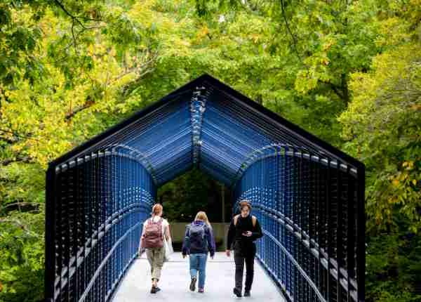 Students walk over a blue bridge among green trees.  